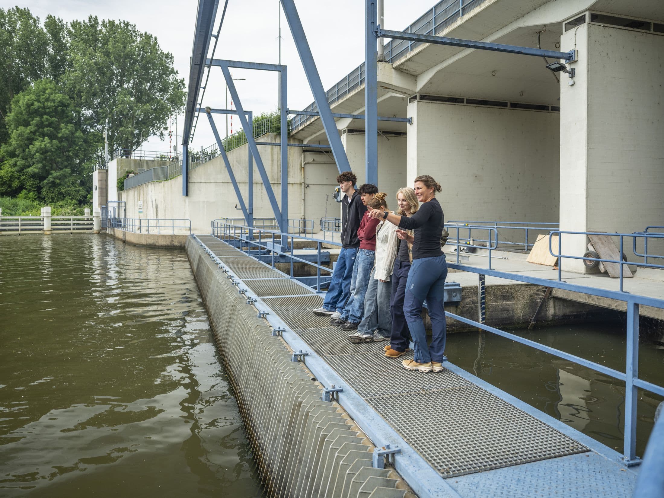Studenten en docent op de loopbrug van een gemaal, met het water ernaast