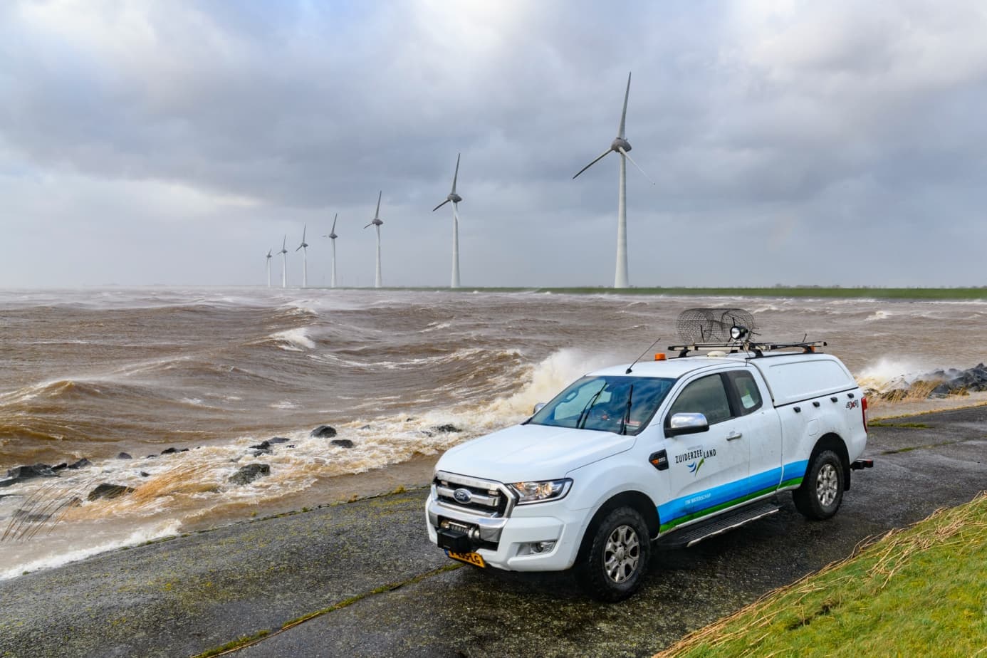Bedrijfswagen op een dijk met windmolens op de achtergrond